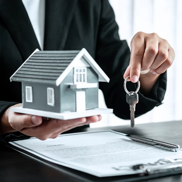 A woman presenting both a house model and key to a new homeowner.