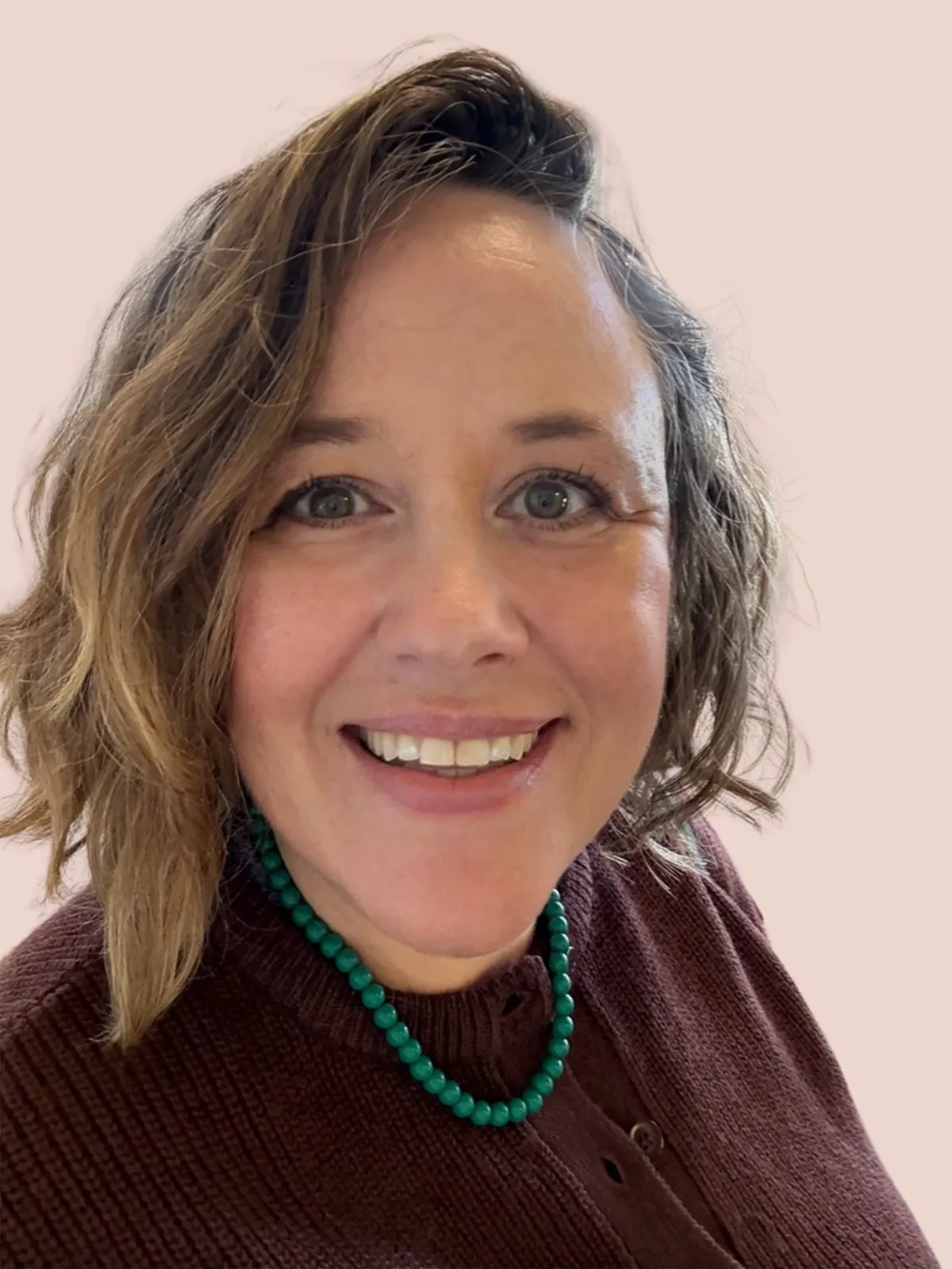 Picture of Emily Wilkinson, a woman with wavy hair wearing glasses and a black sweater. Mint green background. 
