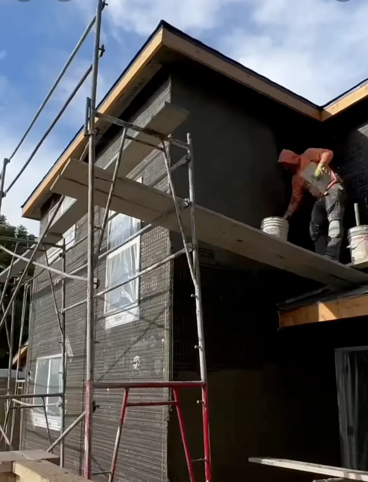Man with orange shirt working on new construction stucco for a house 