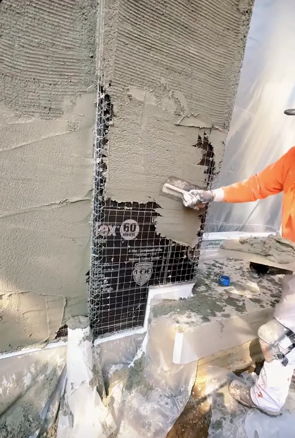 man with orange shirt installing new stucco on a wall
