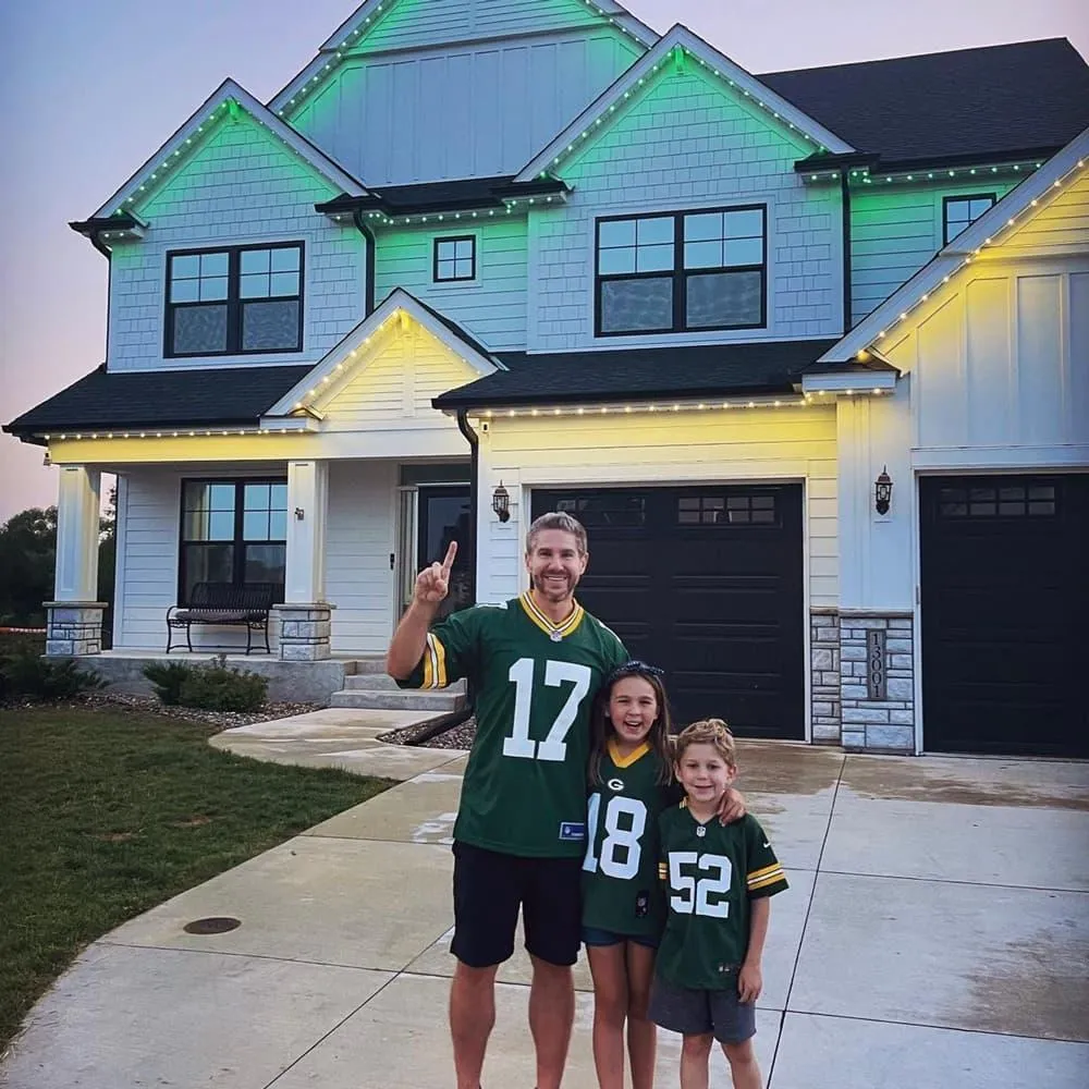 Dad with two kids in Greenbay Packers jersey in front of house with Game Day LED lighting