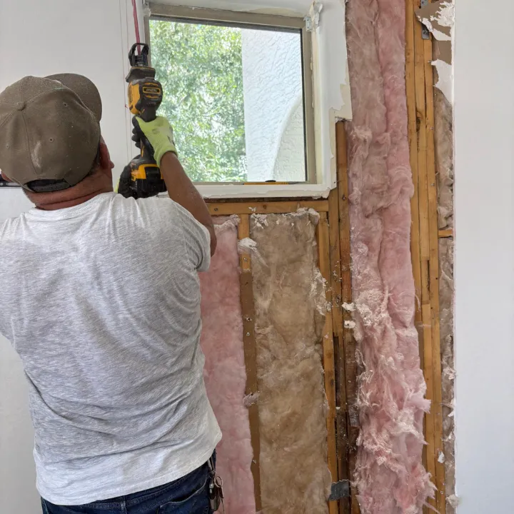 Technician removing drywall to expose wall cavity insulation during Phoenix water damage repair