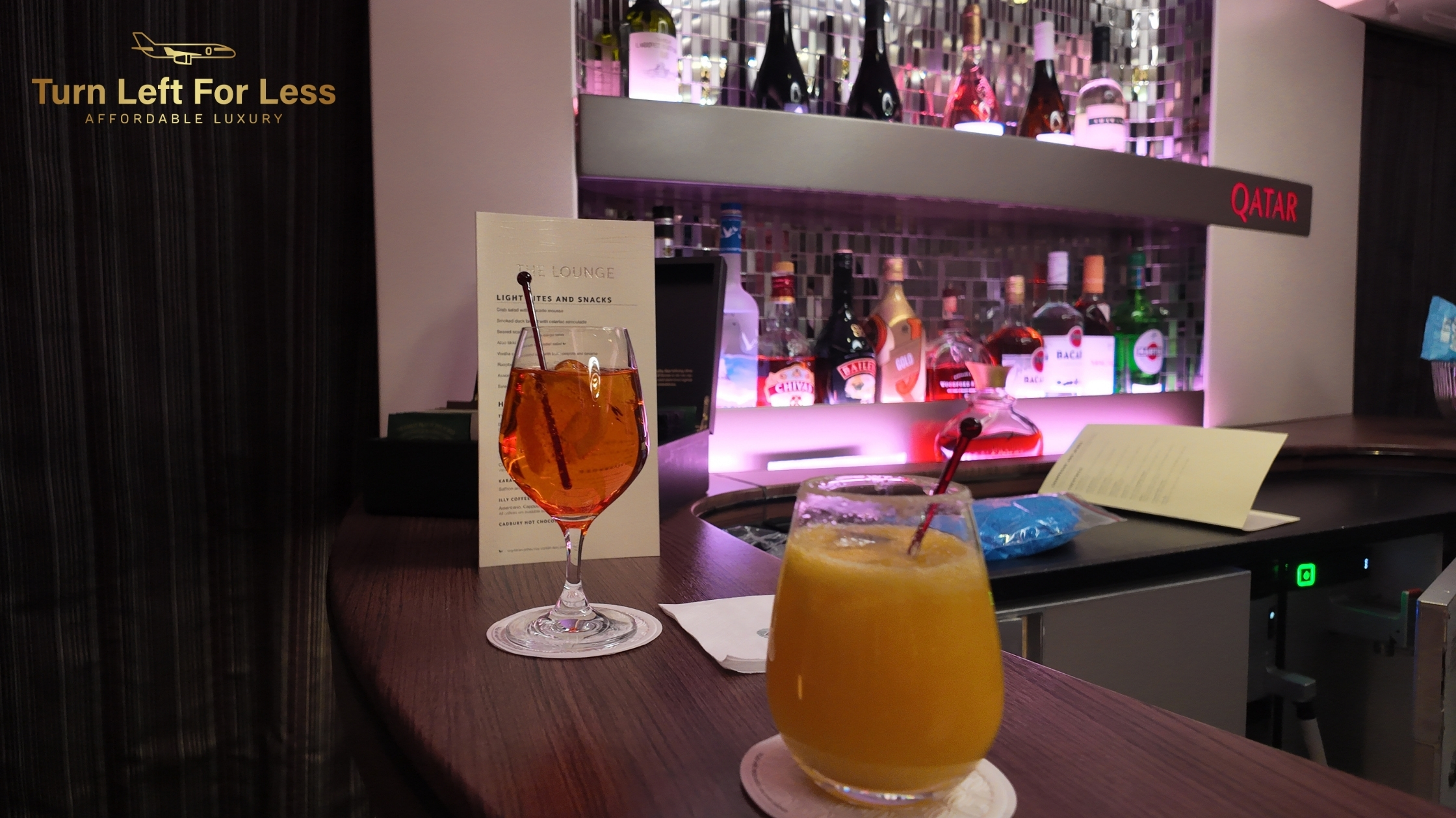 two cocktails on a wooden counter under Turn Left For Less signage