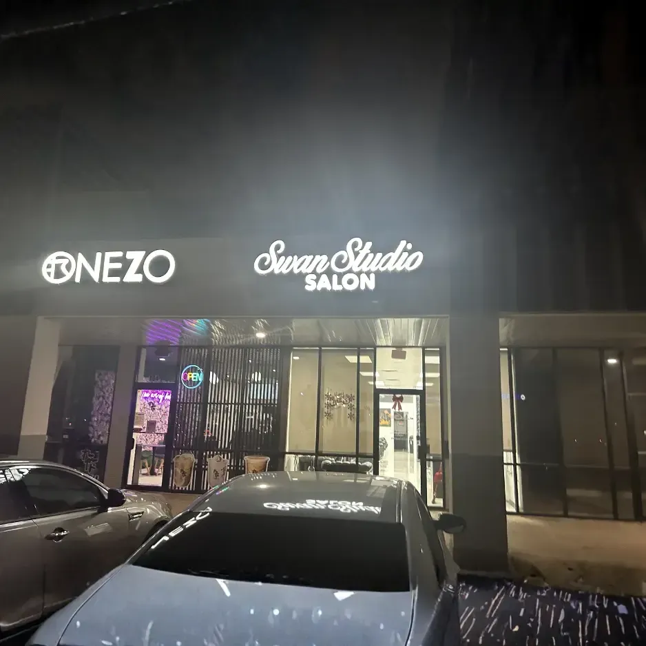 Nighttime view of a retail building featuring illuminated channel letter signs for ONEZO and Swan Studio Salon