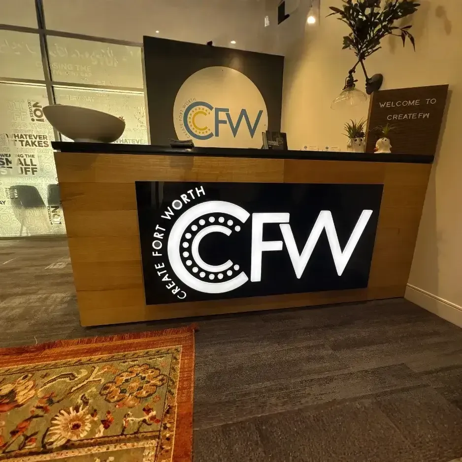 Modern wood-paneled reception desk featuring an illuminated black and white 'Create Fort Worth' (CFW) logo in a professional office lobby