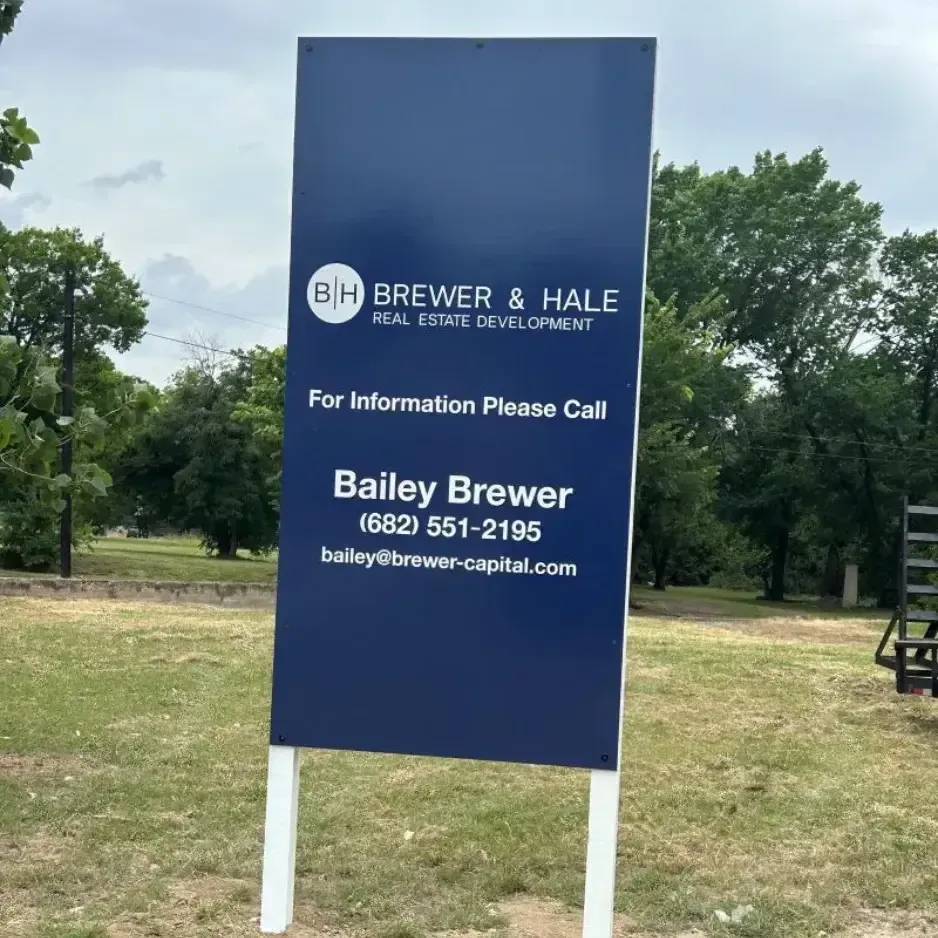 Large blue pylon real estate sign for Brewer & Hale Real Estate Development, featuring contact information for Bailey Brewer and set against a background of green trees