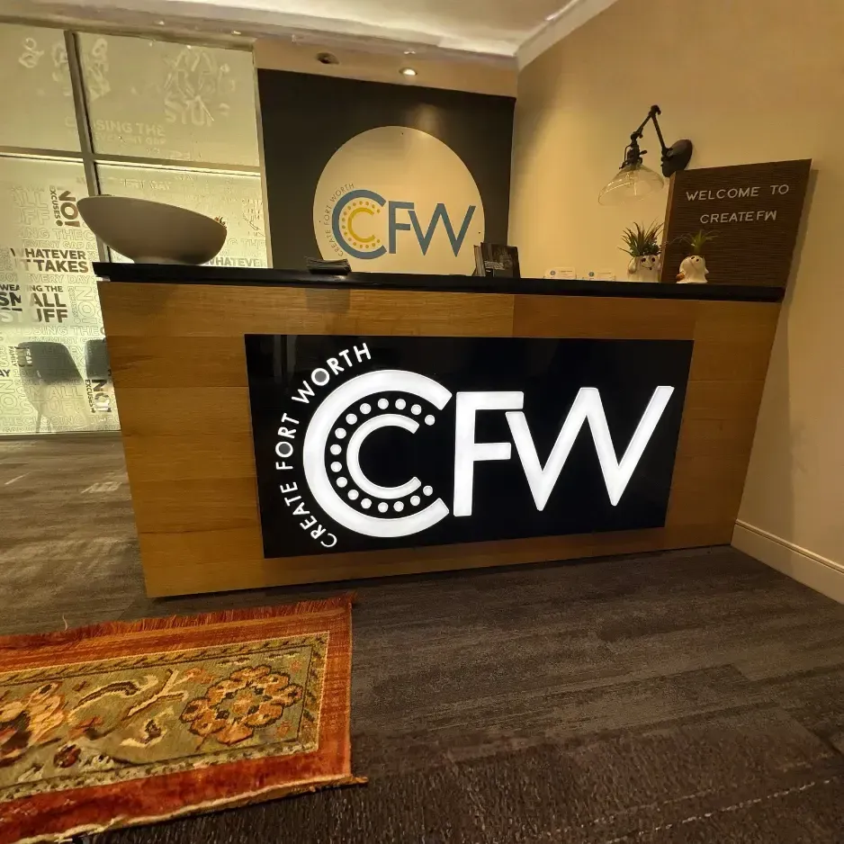Backlit circular lobby sign for CFW mounted on a wooden reception desk in a professional office interior