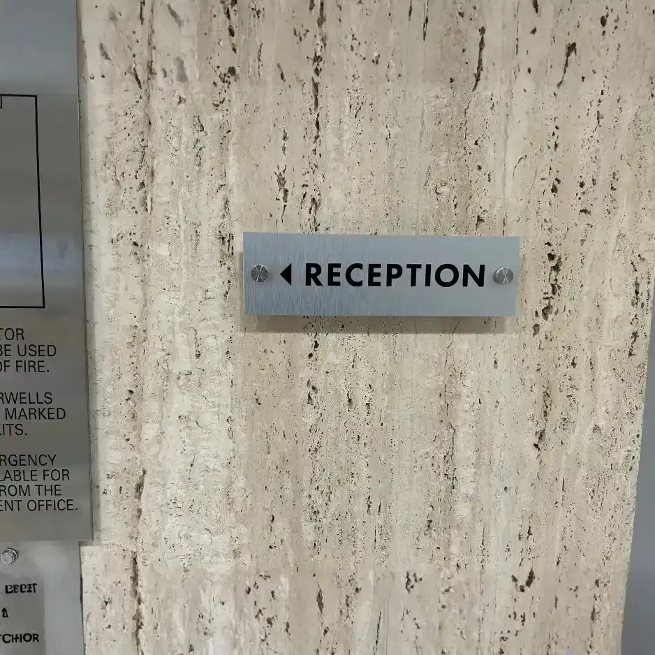 A sleek silver directional sign with black lettering indicating the way to 'Reception' mounted on a textured stone wall