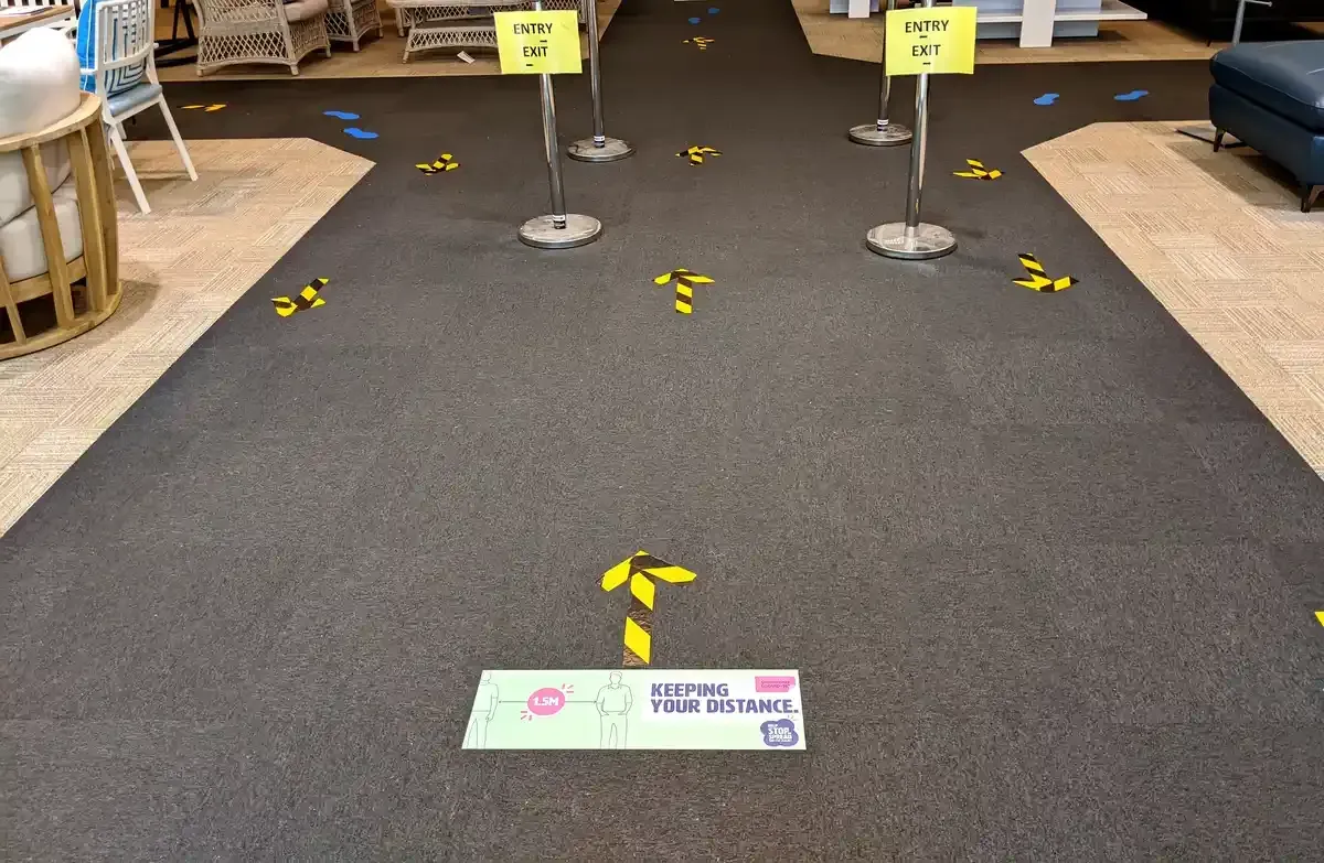 Social distancing floor graphics and yellow arrow decals installed in a retail showroom for customer wayfinding
