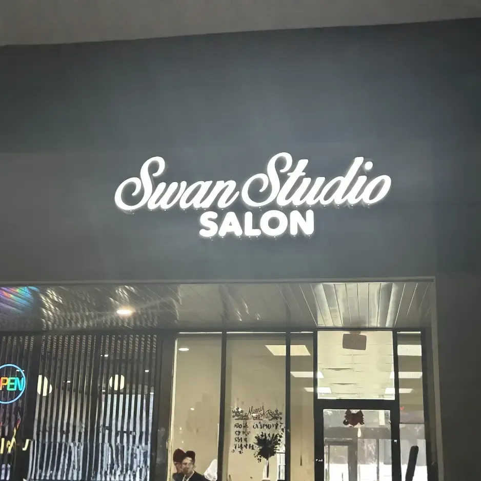 Illuminated white channel letter signage for 'Swan Studio Salon' mounted on a dark grey storefront above a glass entrance