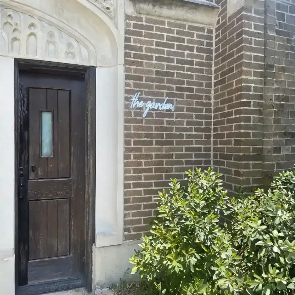 Elegant white dimensional script lettering for 'the garden' installed on a classic brick building exterior next to a wooden door