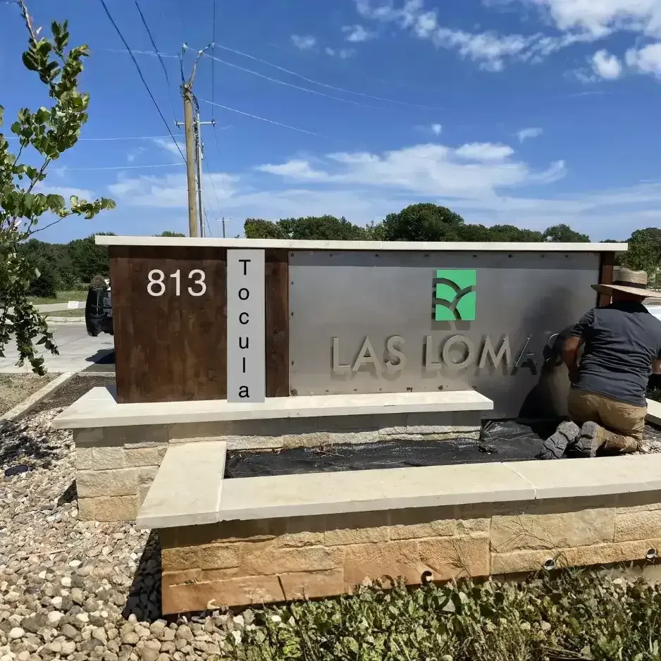 Installation of a modern stone and wood-textured exterior monument sign for a business address in North Texas