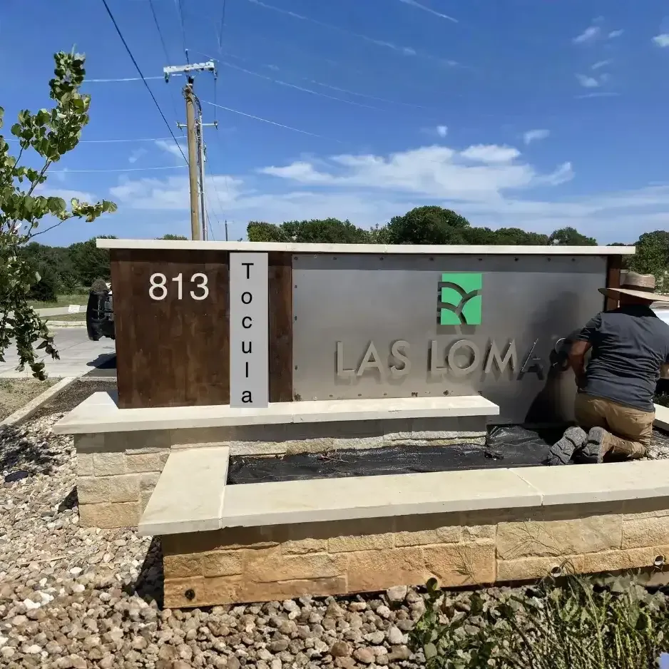 Technicians installing a custom modern stone monument sign for Las Lomas with dimensional lettering and decorative wood accents