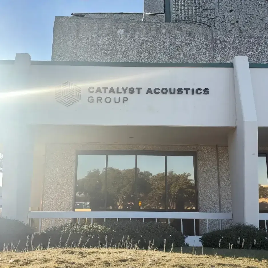 A modern wall-mounted logo sign for Catalyst Acoustics Group positioned above the entrance of a contemporary glass and concrete office facility