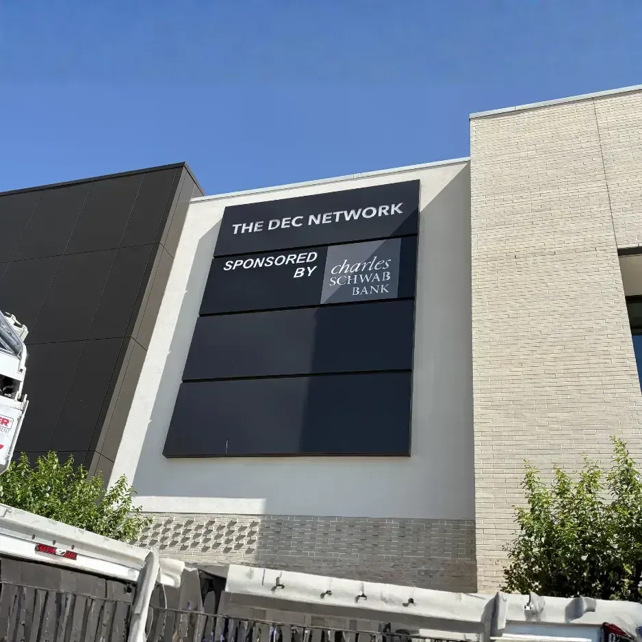 Large-scale exterior building sign for The DEC Network, featuring 'Sponsored by' branding on a modern multi-story facility