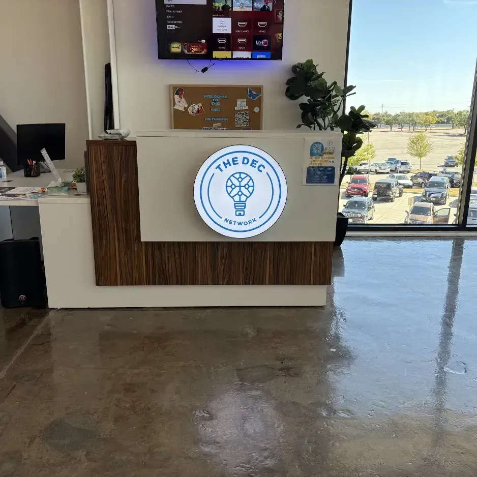 Clean, modern reception area featuring a circular illuminated 'The DEC' lobby sign mounted on a white desk with wood accents
