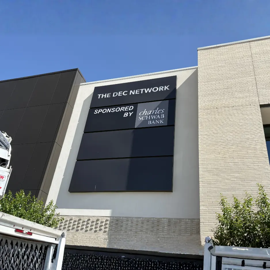 Large-scale exterior building sign for The DEC Network, featuring 'Sponsored by Charles Schwab Bank' branding on a modern multi-story office facility