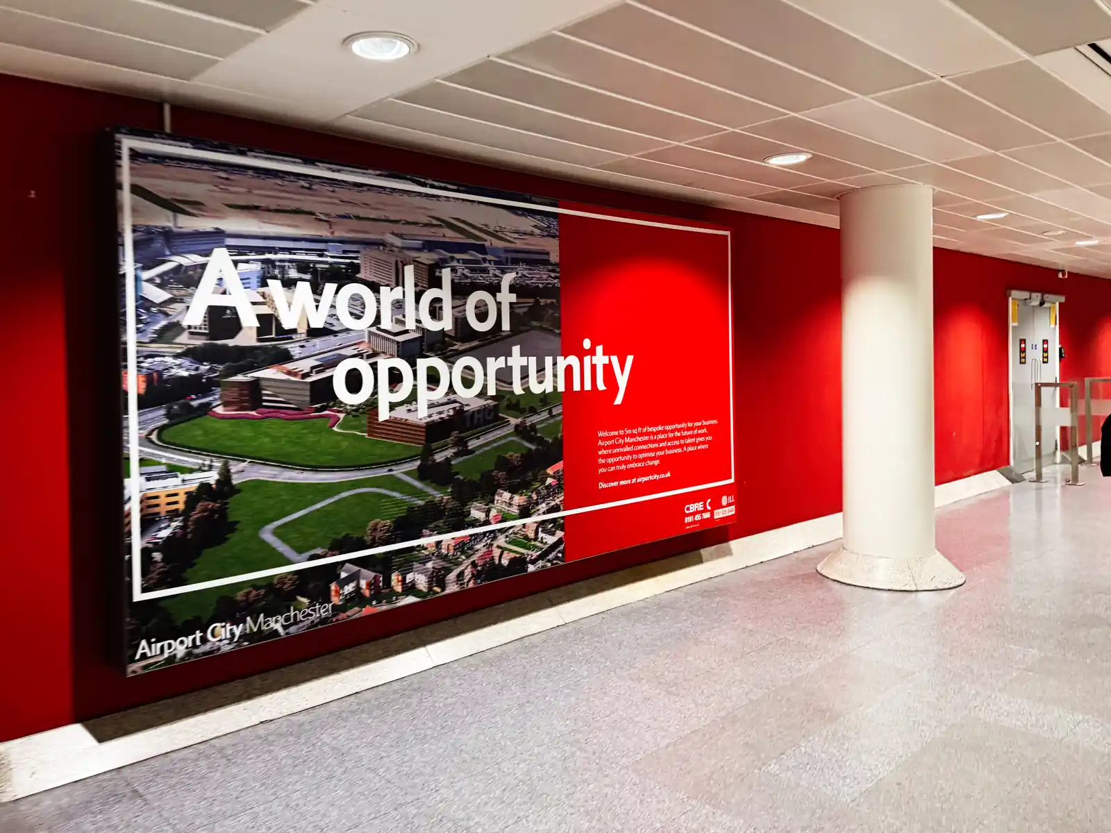 A large, red illuminated wall graphic in a modern office hallway displaying "A world of opportunity" alongside high-quality campus imagery