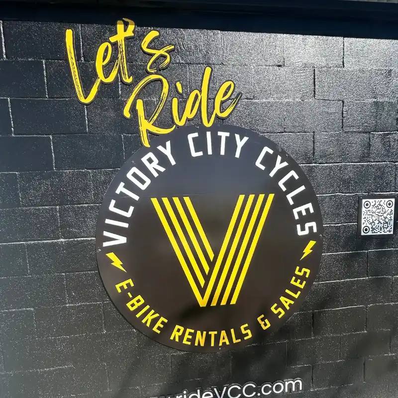  Large yellow and white hand-painted e-bike rental logo mural for Victory City Cycles on a dark exterior brick wal