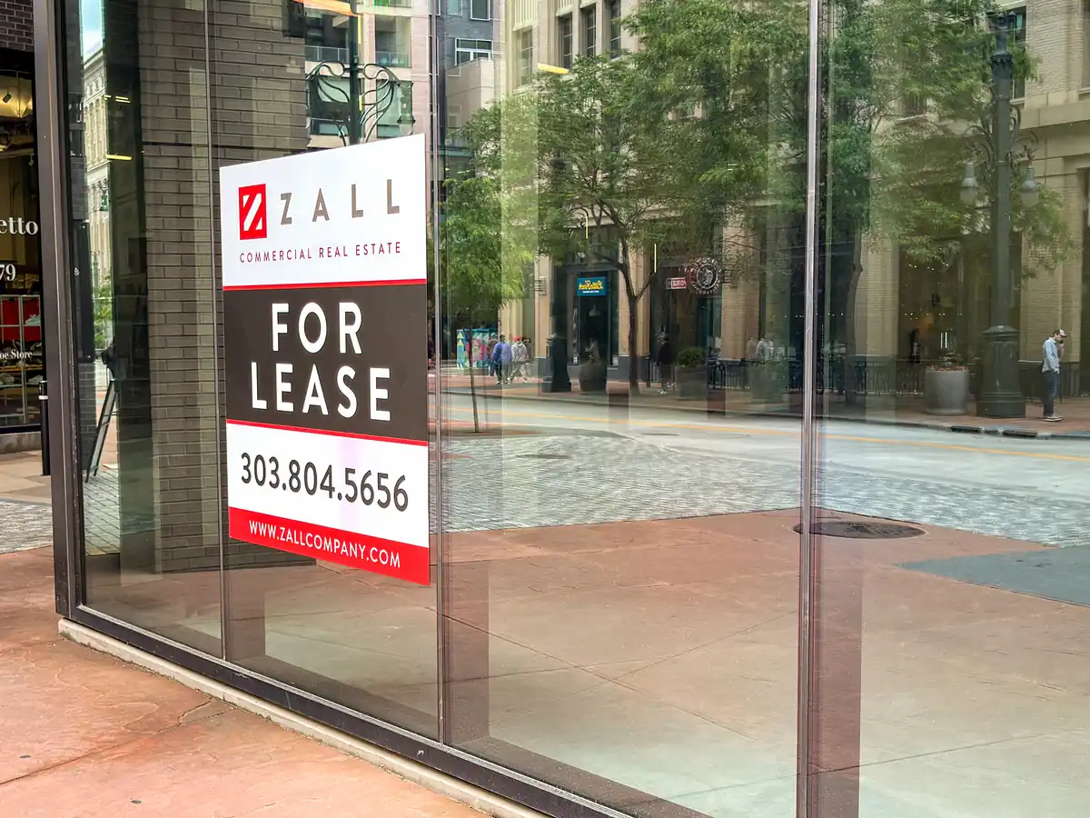 A professional "FOR LEASE" vinyl window sign with red and white branding applied to a clean glass storefront in a commercial area