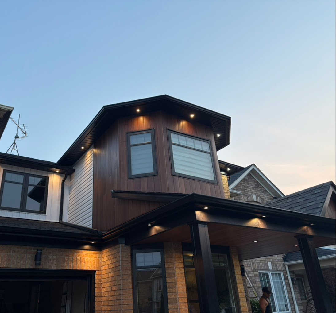 Modern exterior home renovation in Toronto by Infinity Gutters & Exteriors, featuring vertical wood-look siding, sleek black seamless gutters, and glowing warm soffit lighting.