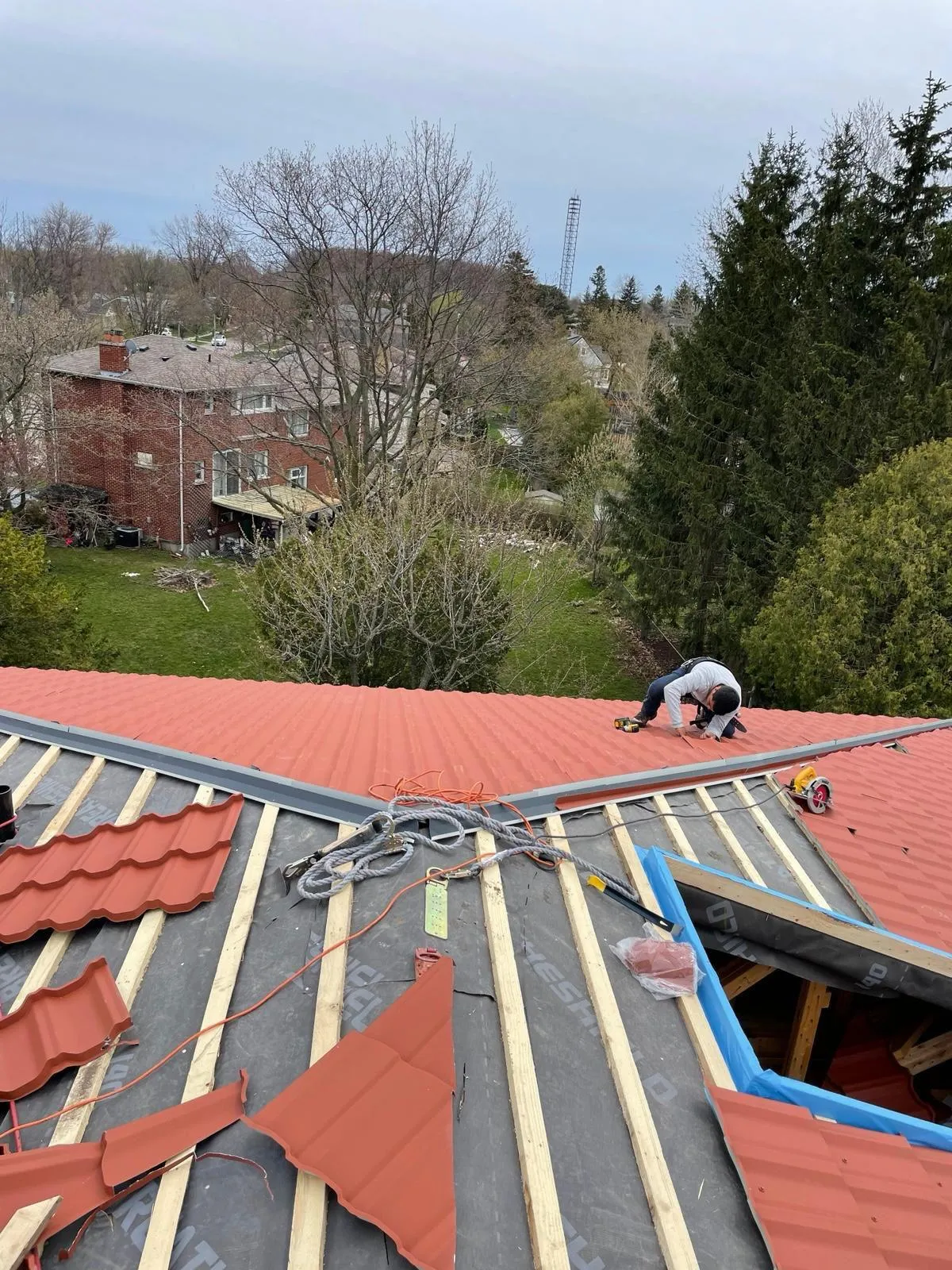 Contractor installing red metal roofing panels on a residential roof during a custom metal roof installation project by Infinity Gutters in Ontario