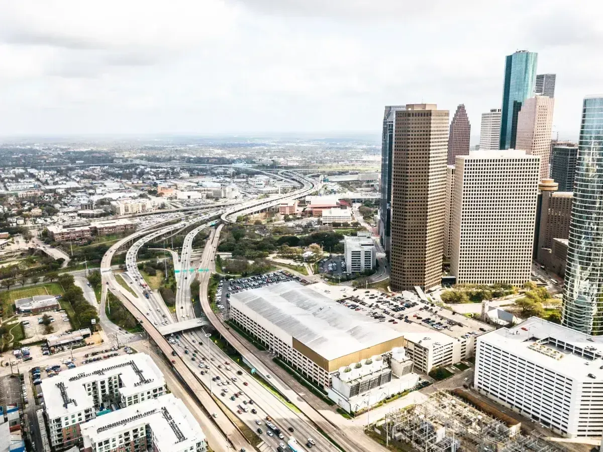 Aerial view of a major city downtown with tall skyscrapers, busy freeways, and a large parking structure.