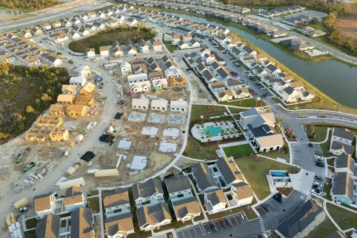Aerial view of a large, dense housing development with a construction site, community pool, and retention pond.