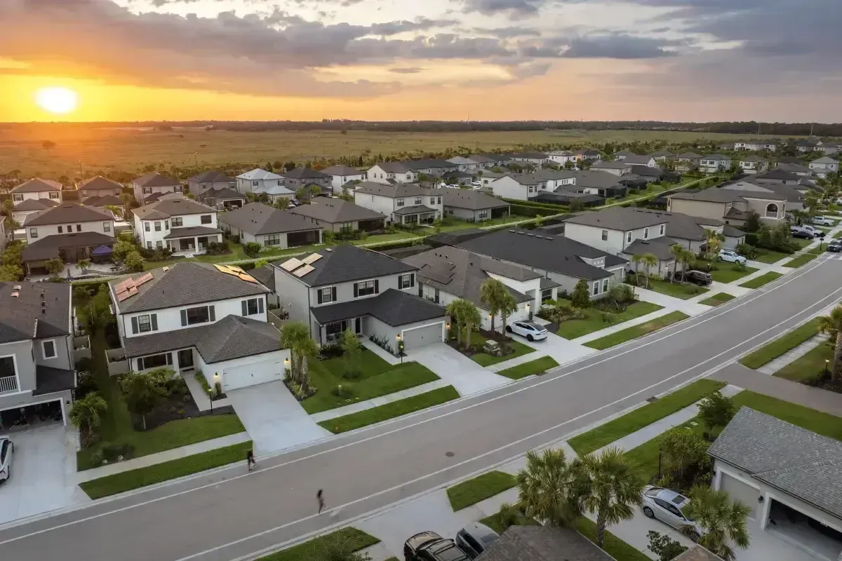 Drone shot of a Florida-style residential area with uniform homes and lush green yards during golden hour.