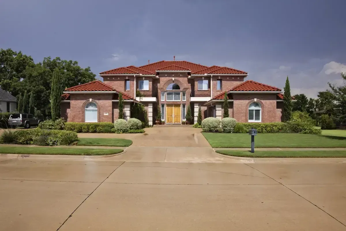 Luxurious red brick and stucco two-story home with a clay tile roof, arched windows, and circular driveway.
