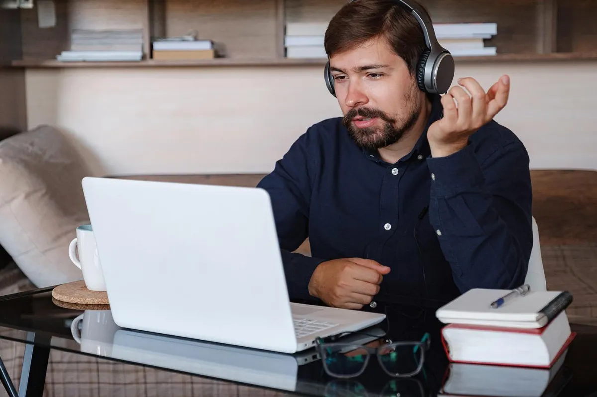 Image of a man with headphones on in front of a laptop having a conversation