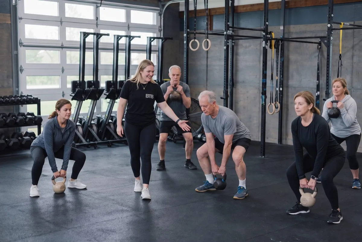 A small Stronger for Longer class doing coached kettlebell squats at Between The Bumpers in Stittsville