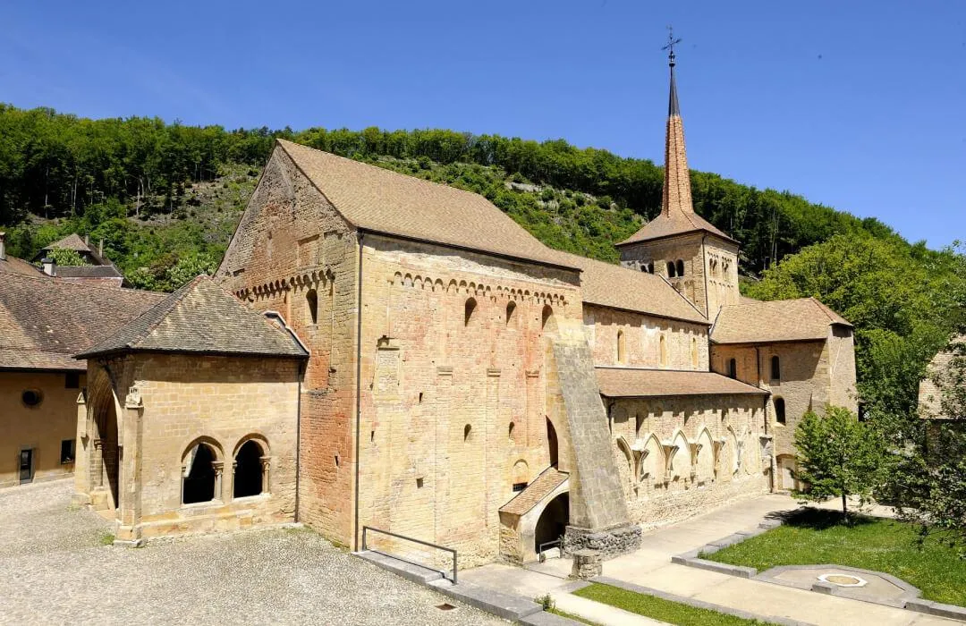 Romainmôtier Abbey surrounded by Jura hills under blue sky