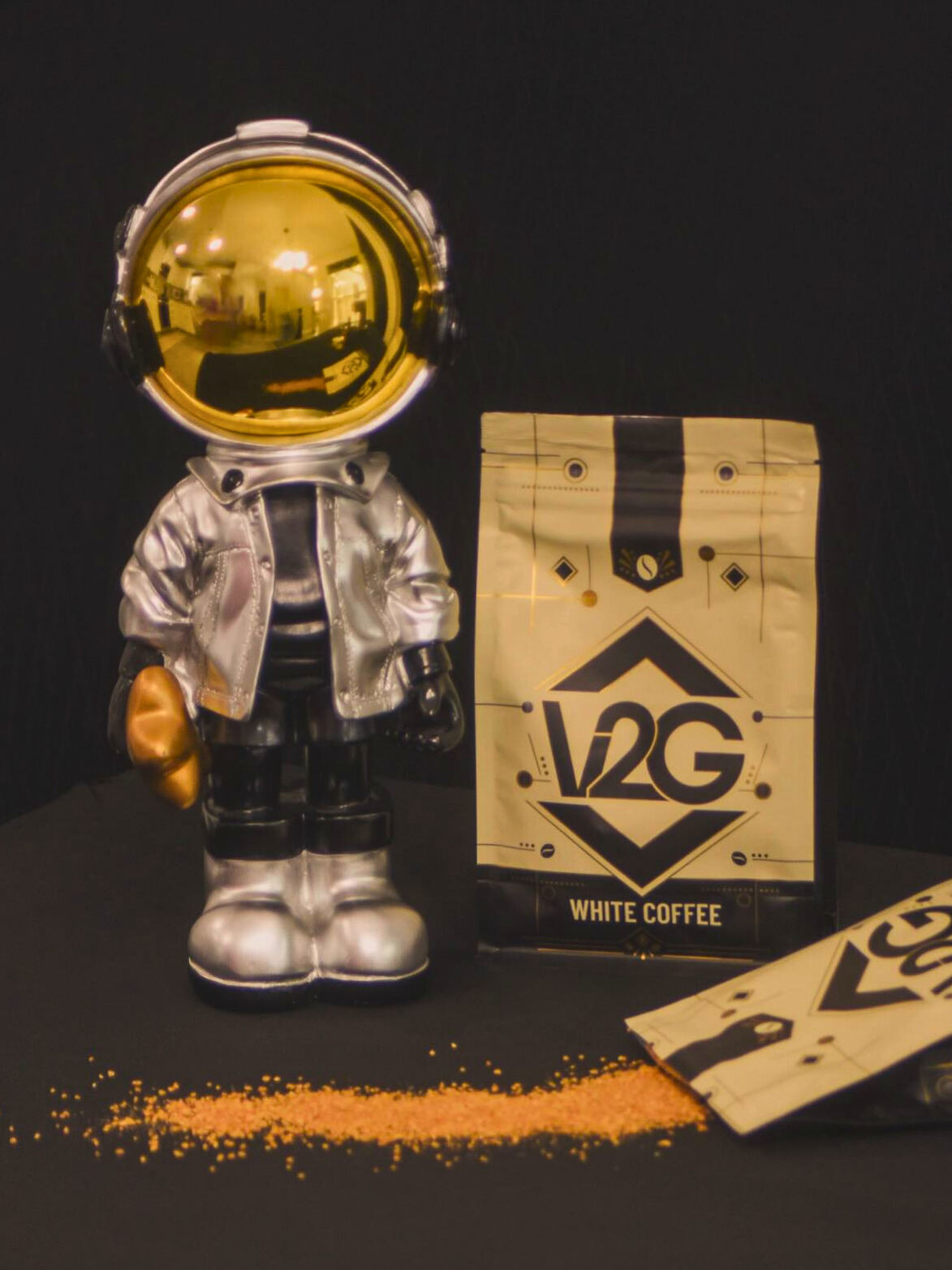 Vibes 2 Go white coffee packaging displayed beside a gold-helmet astronaut figurine with white coffee grounds on a black table.