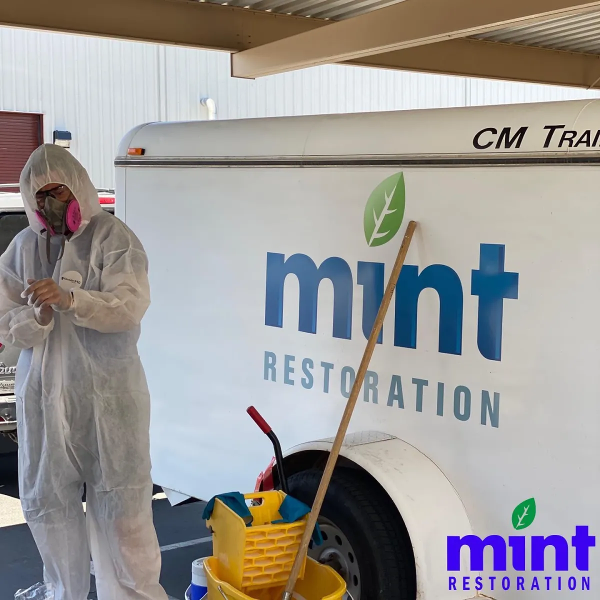 A person in a white protective suit and respirator stands next to a trailer