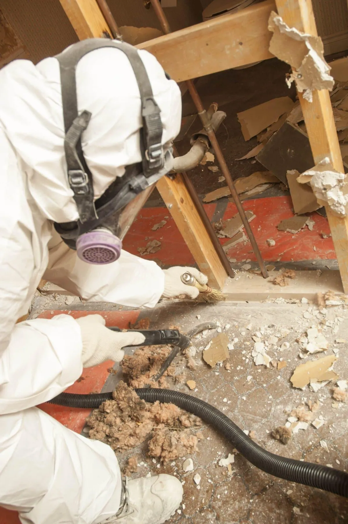 A person in a white protective suit and mask vacuuming asbestos 