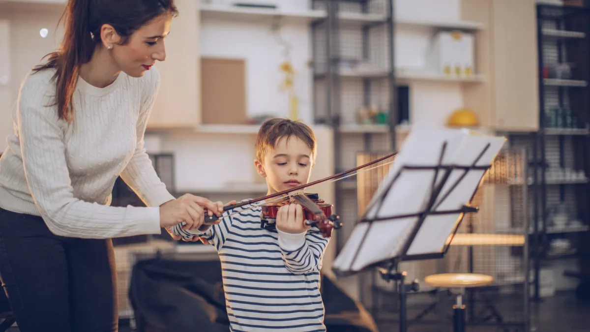 Two children playing an upright piano together, one focusing on the lower keys and the other on the higher ones. Both kids are smiling, engaged in playing, in a cozy room with warm lighting. The scene highlights the joy of collaborative music-making.