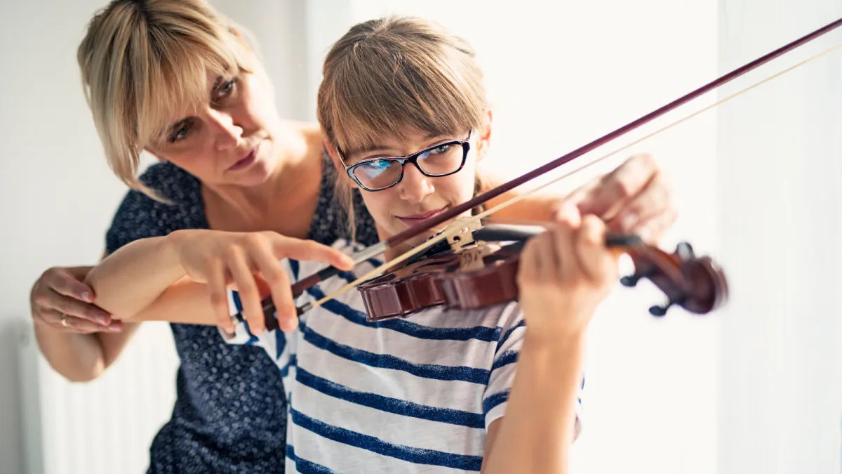 An adult, dressed in a colorful long sleeve and eyeglasses, sits attentively at a sleek digital keyboard, their fingers moving gracefully over the keys. The soft glow of a tilt light bathes the scene, casting an inviting, warm ambiance around them. 