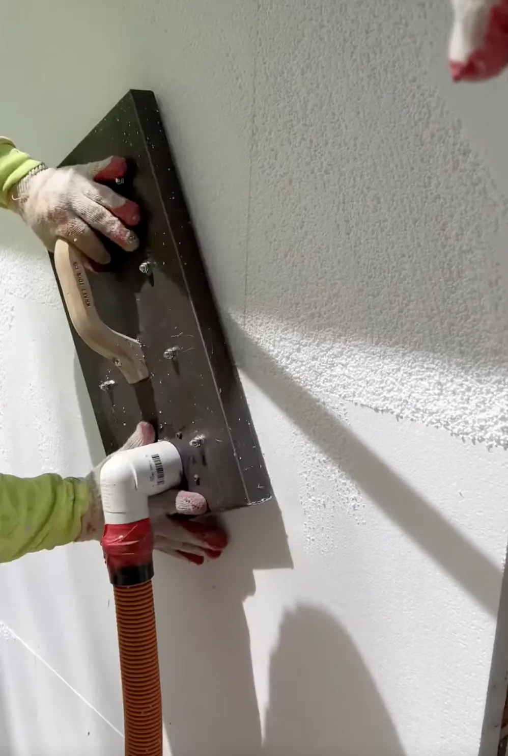 Man using a machine to create smooth stucco on a white wall