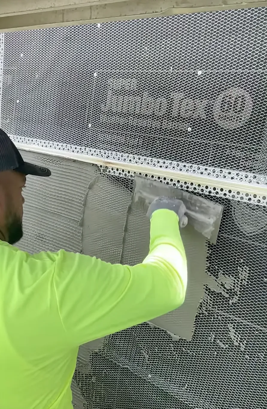 Man with neon green shirt applying new stucco to a house
