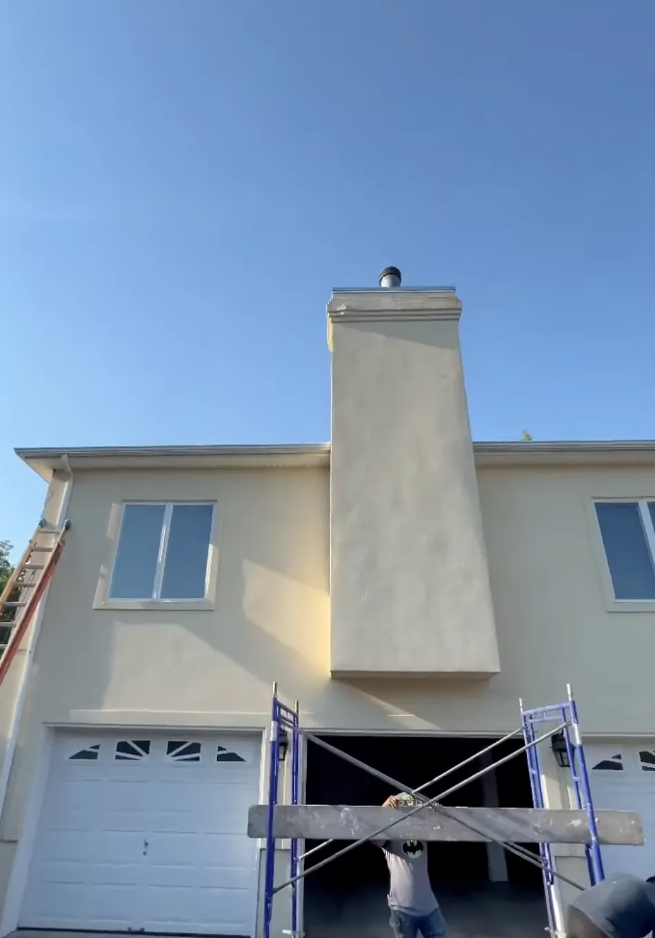 House with tan stucco with two garage doors and men using ladders 