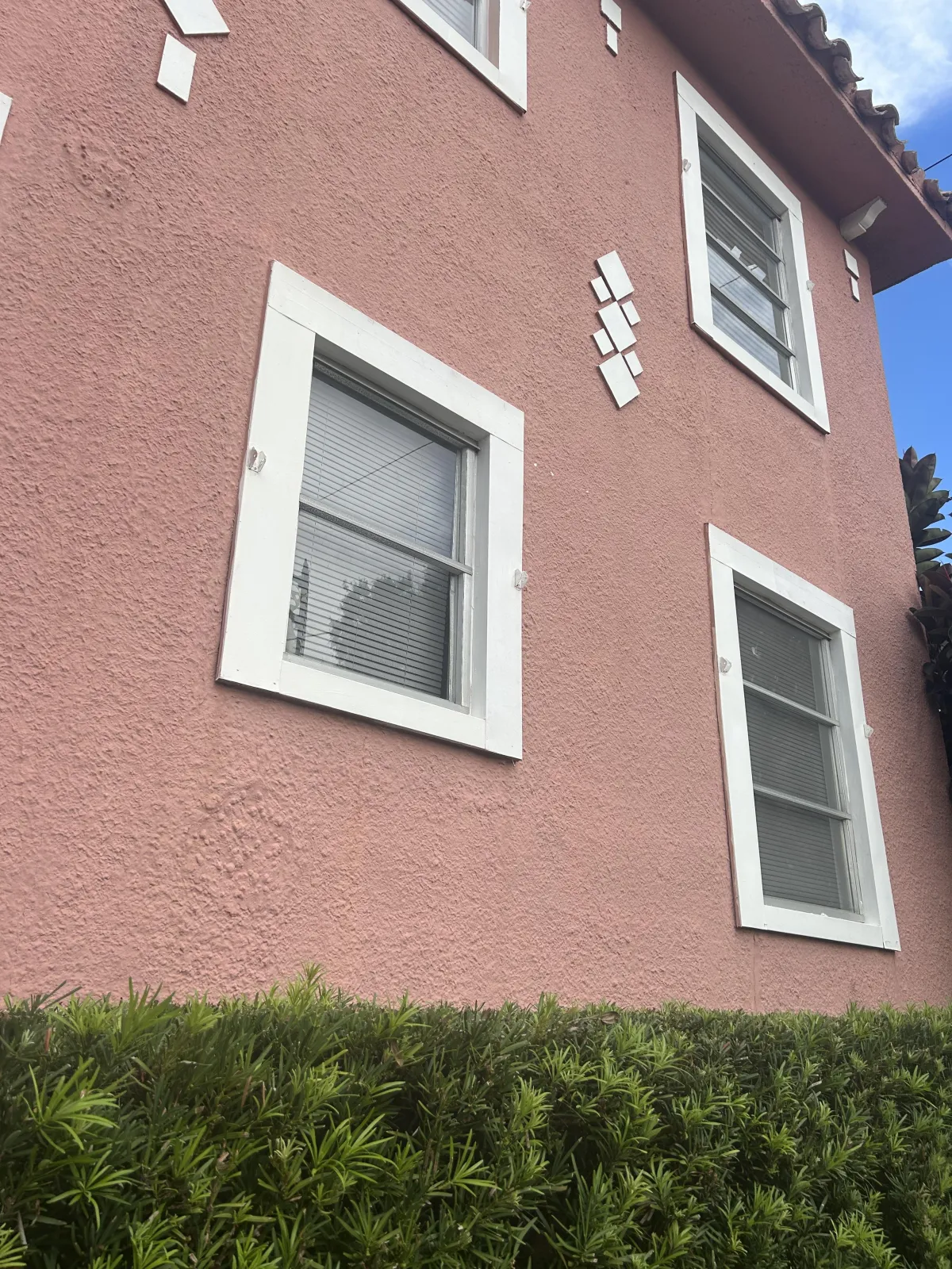 House with pink stucco & 4 windows with shrubs underneath