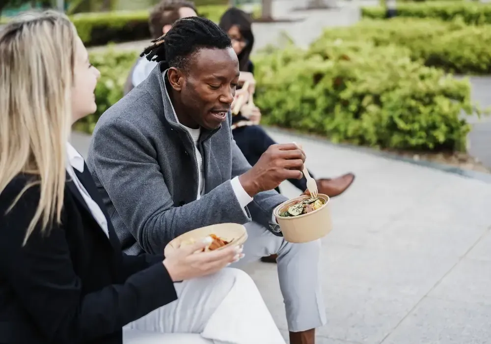 Two people sitting outdoors and eating from bowls.