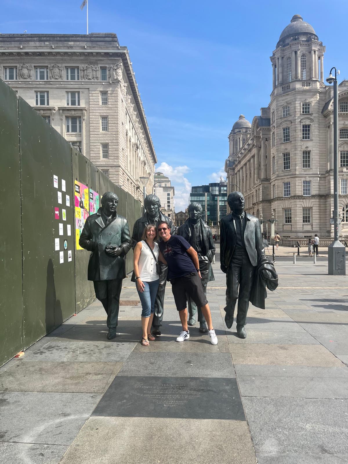 Image and Jo and her husband sood in front of a Beatles Statue in Liverpool.