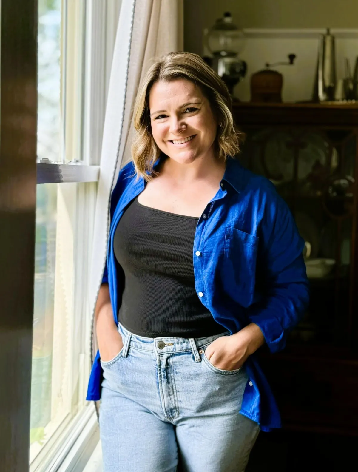 therapist for postpartum and toddler moms standing at window with hands in pockets and warm smile