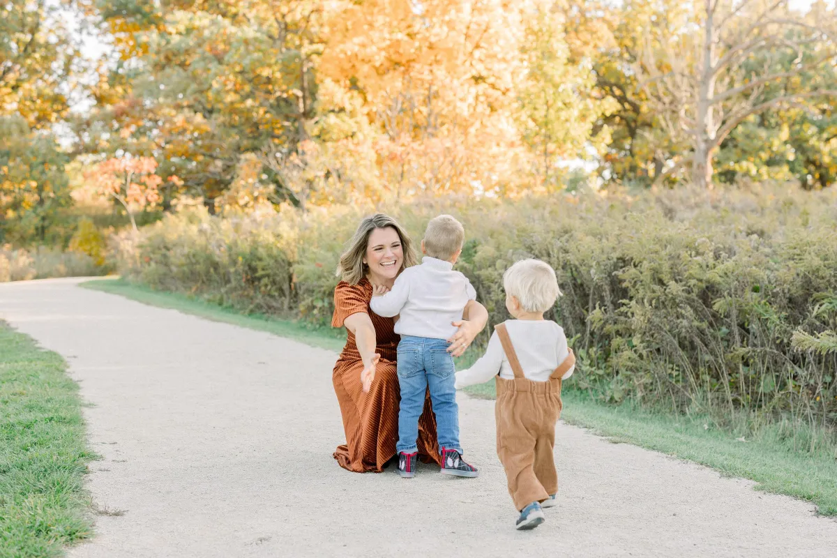 mother crouching down with arms open to hug two blonde haired boys running toward her