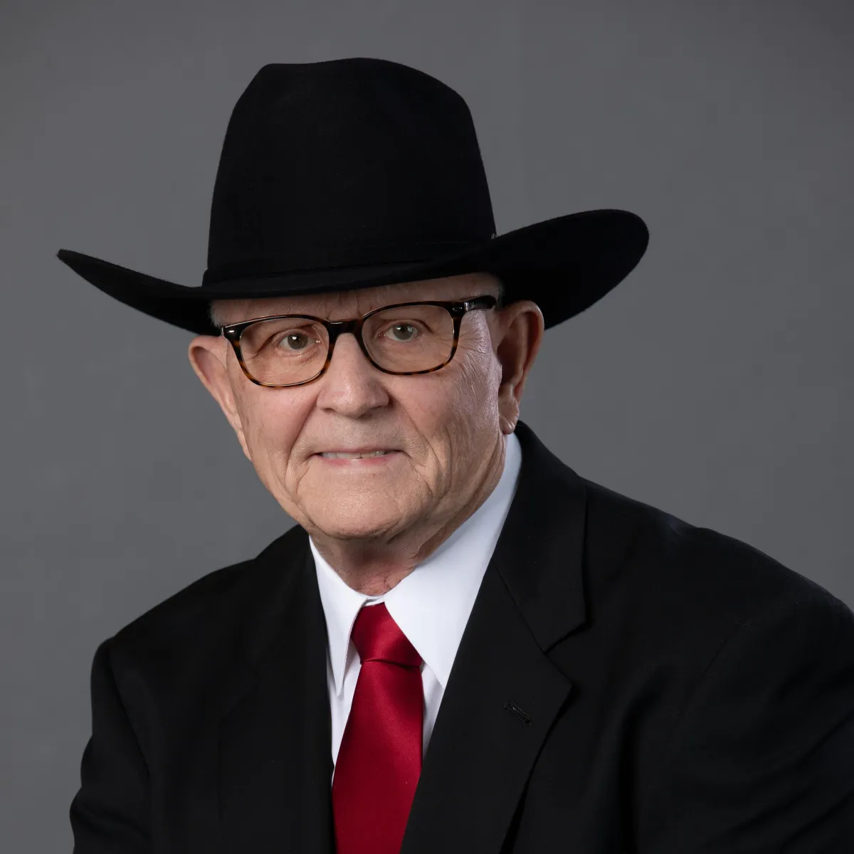 Headshot of an older man wearing a black cowboy hat and glasses
