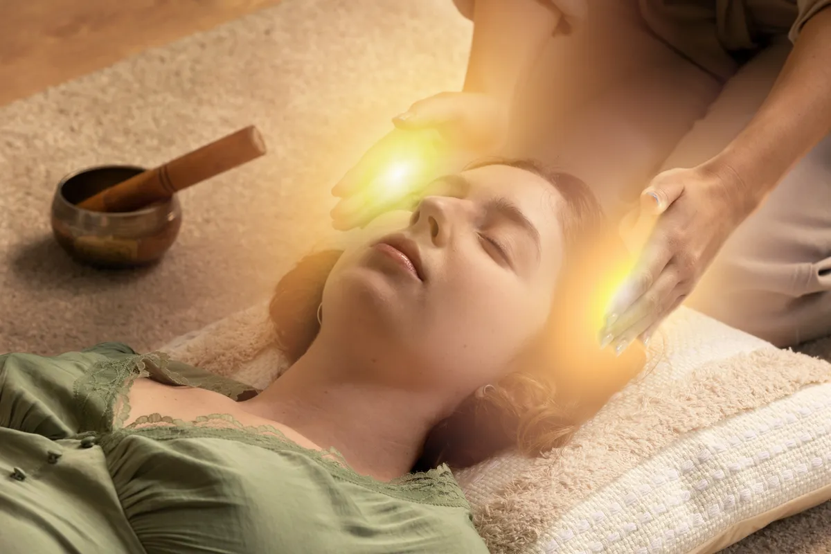 Close-up photograph of a woman lying down with eyes closed, appearing peaceful and relaxed, possibly receiving a treatment.
