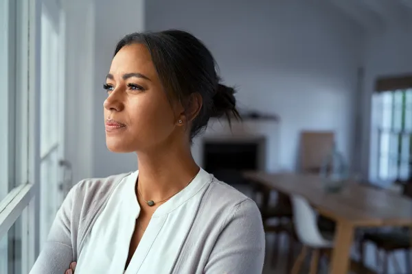 Woman looking thoughtfully out of a window at home, reflecting emotional disconnection and lack of intimacy in her sex life
