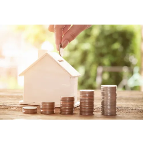 hand putting a coin into a piggy bank that is shaped like a house.  